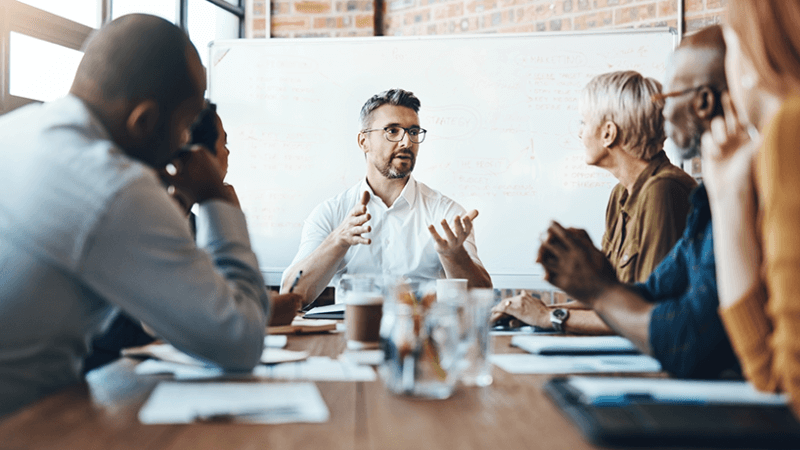 Manager sits at head of table talking to his coworkers