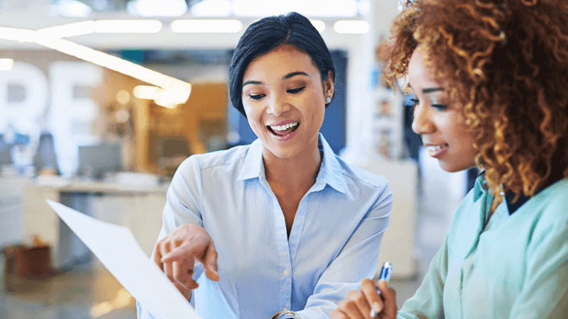 Two women in an office pointing at a paper 