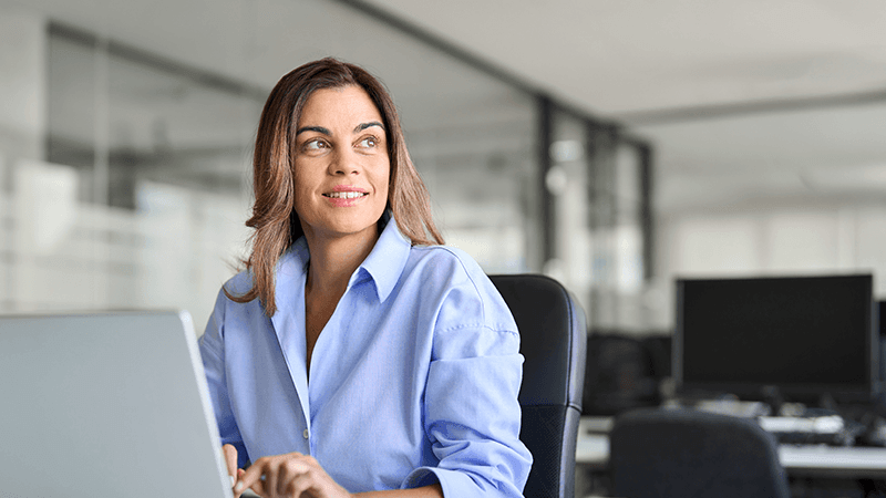 Female executive sits in front of computer in an office, smiling and looking off into the distance