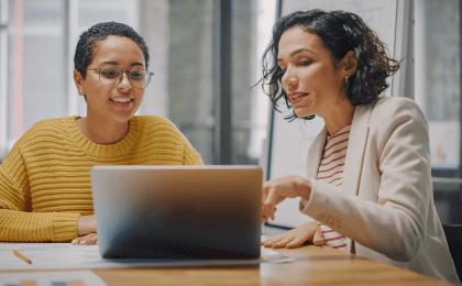 Women at work discussing while looking at a computer screen, main image for blog on the connection between personality assessments and retention rates