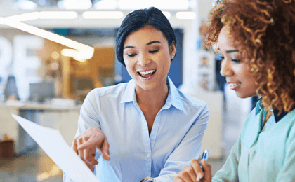 Two women in an office pointing at a paper 