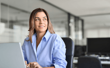 Female executive sits in front of computer in an office, smiling and looking off into the distance