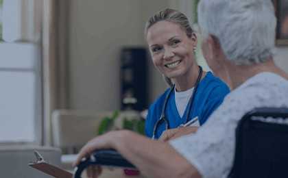 female nurse in blue scrubs smiling at elderly patient